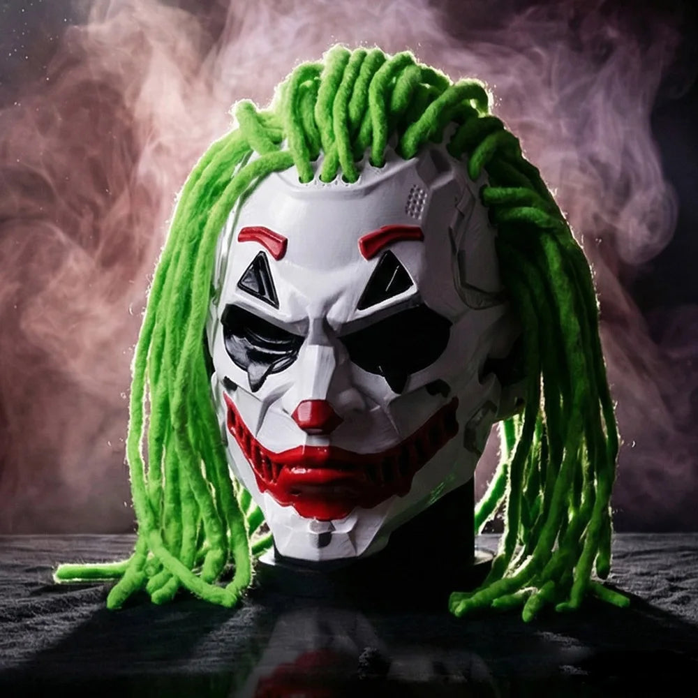 A Joker-style full-face mask with bright green yarn-like hair, a white face, black eye openings, red painted lips and nose, and a dark background with smoky purple lighting.